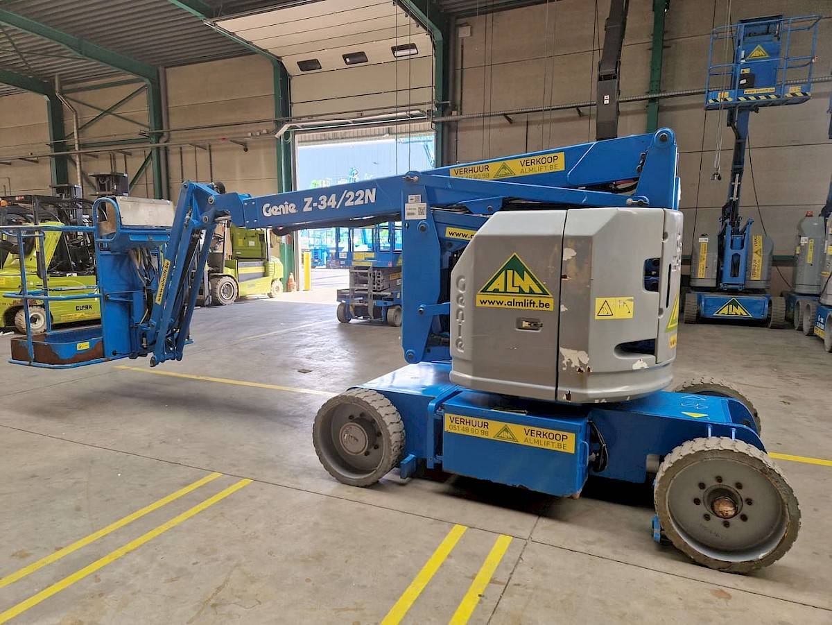 Un bras articulé Genie Z-34/22N bleu, marqué avec LOCATION et VENTE, est dans un entrepôt.
